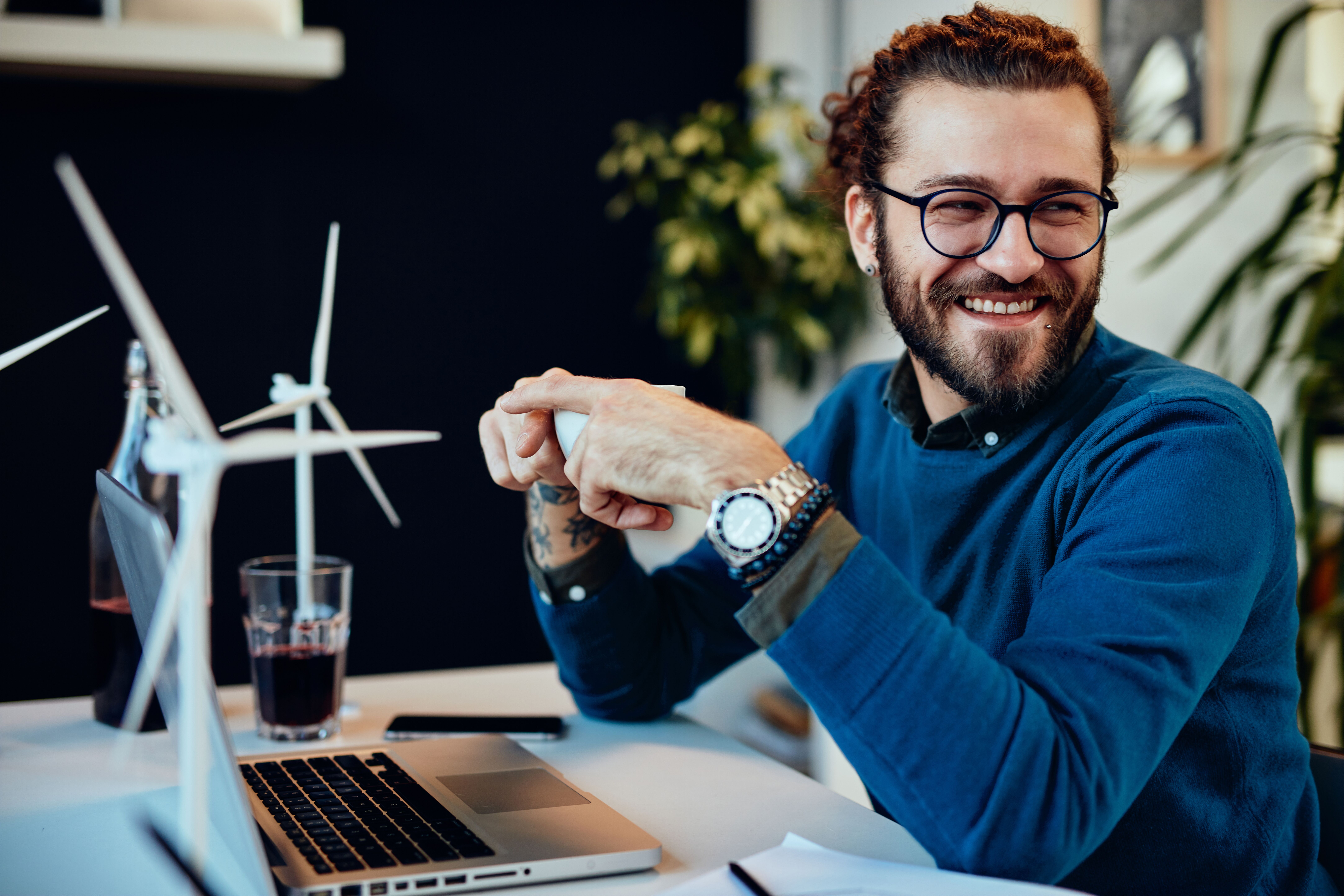 Confident entrepreneur smiling while reviewing financial documents at a desk with a laptop and wind turbine models, symbolizing clarity and sustainability in business planning