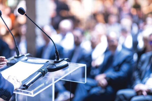 Clear podium with microphones at a business event, representing Michelle M. Delker’s TBBW “20 Questions” feature by Jo-Lynn Brown.