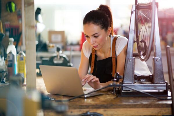Focused entrepreneur in a workshop reviewing a laptop, surrounded by tools and supplies, representing hands-on financial planning and budgeting for growth
